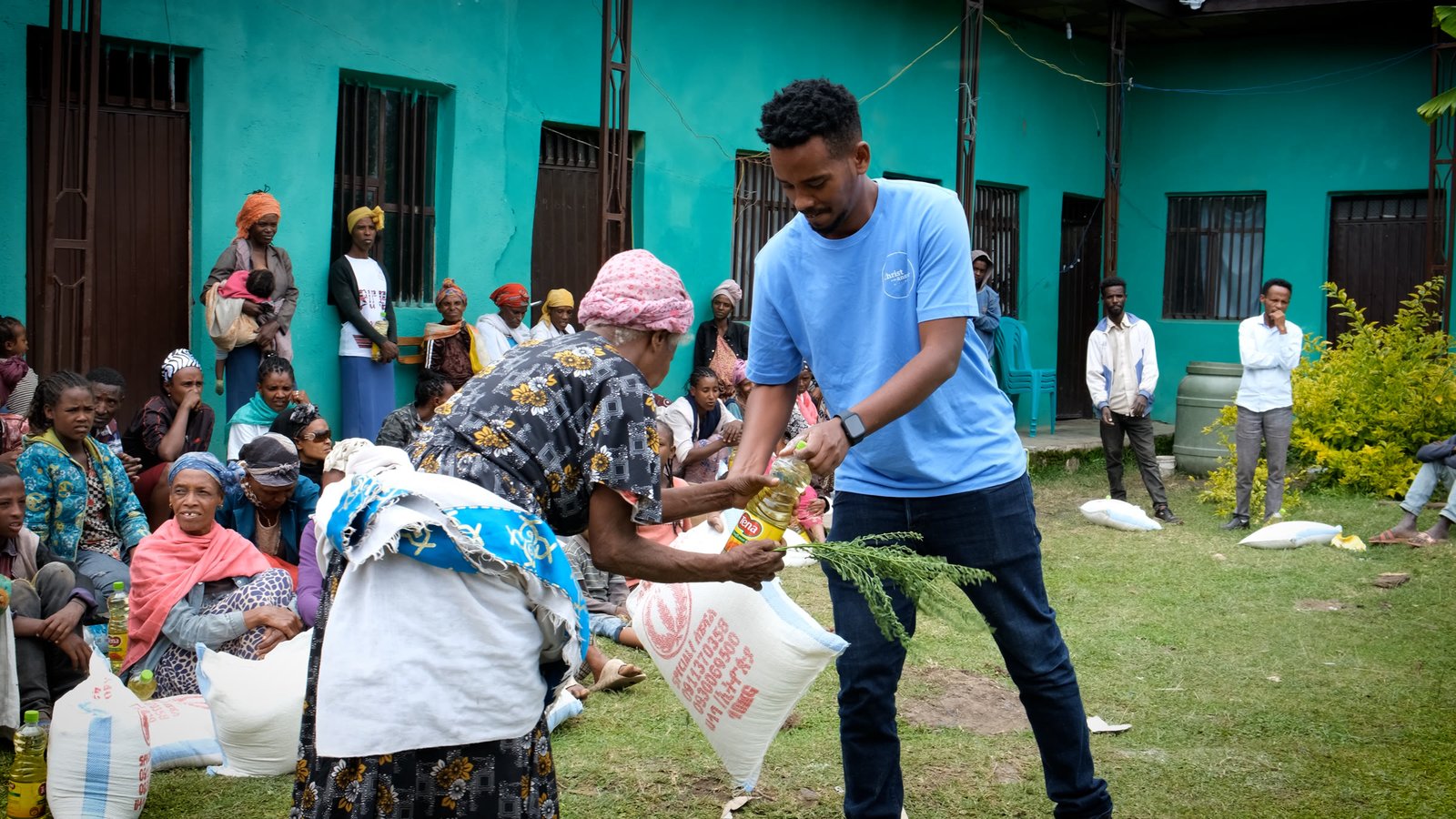 A local team member handing cooking oil and a food sack to a woman.