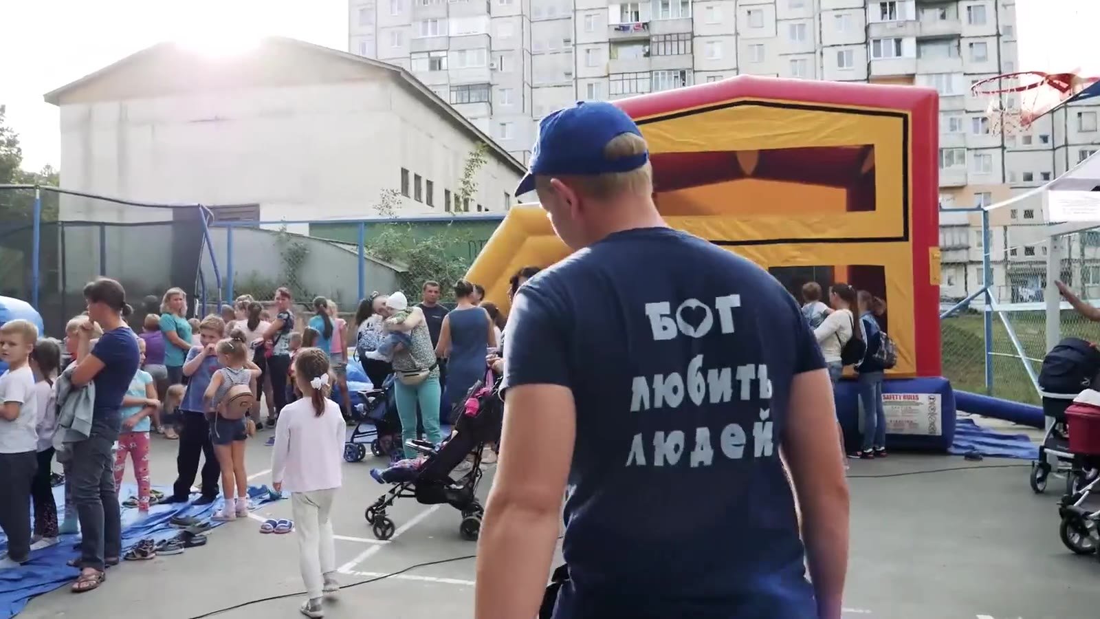 A volunteer whose T-shirt reads “God loves people” in Ukrainian, walking among families at an outdoor community event.